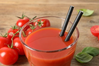 Photo of Tasty tomato juice in glass, basil leaves and fresh vegetables on wooden table, closeup