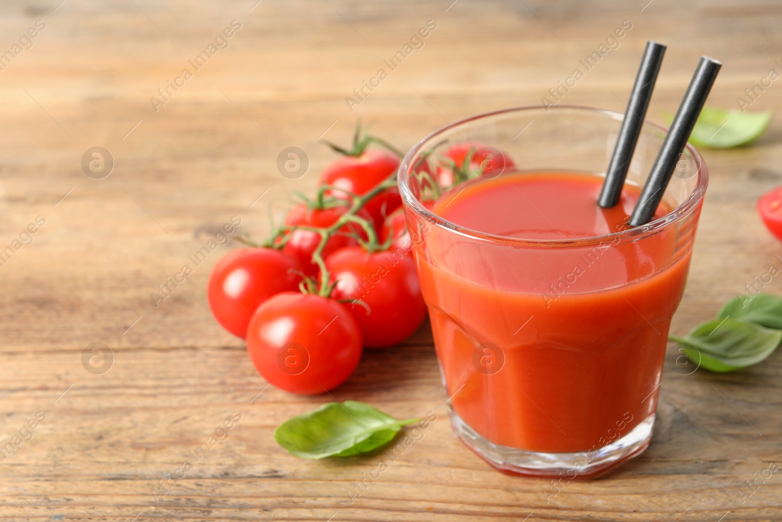 Photo of Tasty tomato juice in glass, basil leaves and fresh vegetables on wooden table. Space for text