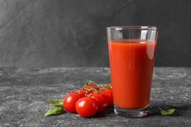 Photo of Tasty tomato juice in glass, basil and fresh vegetables on grey table. Space for text