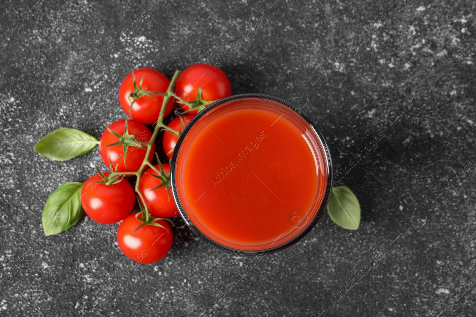 Photo of Tasty tomato juice in glass, basil and fresh vegetables on grey table, top view