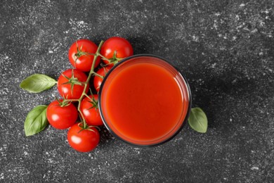 Photo of Tasty tomato juice in glass, basil and fresh vegetables on grey table, top view