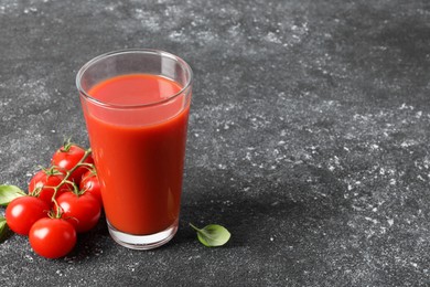 Photo of Tasty tomato juice in glass, basil and fresh vegetables on grey table, space for text