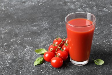 Tasty tomato juice in glass, basil and fresh vegetables on grey table, space for text