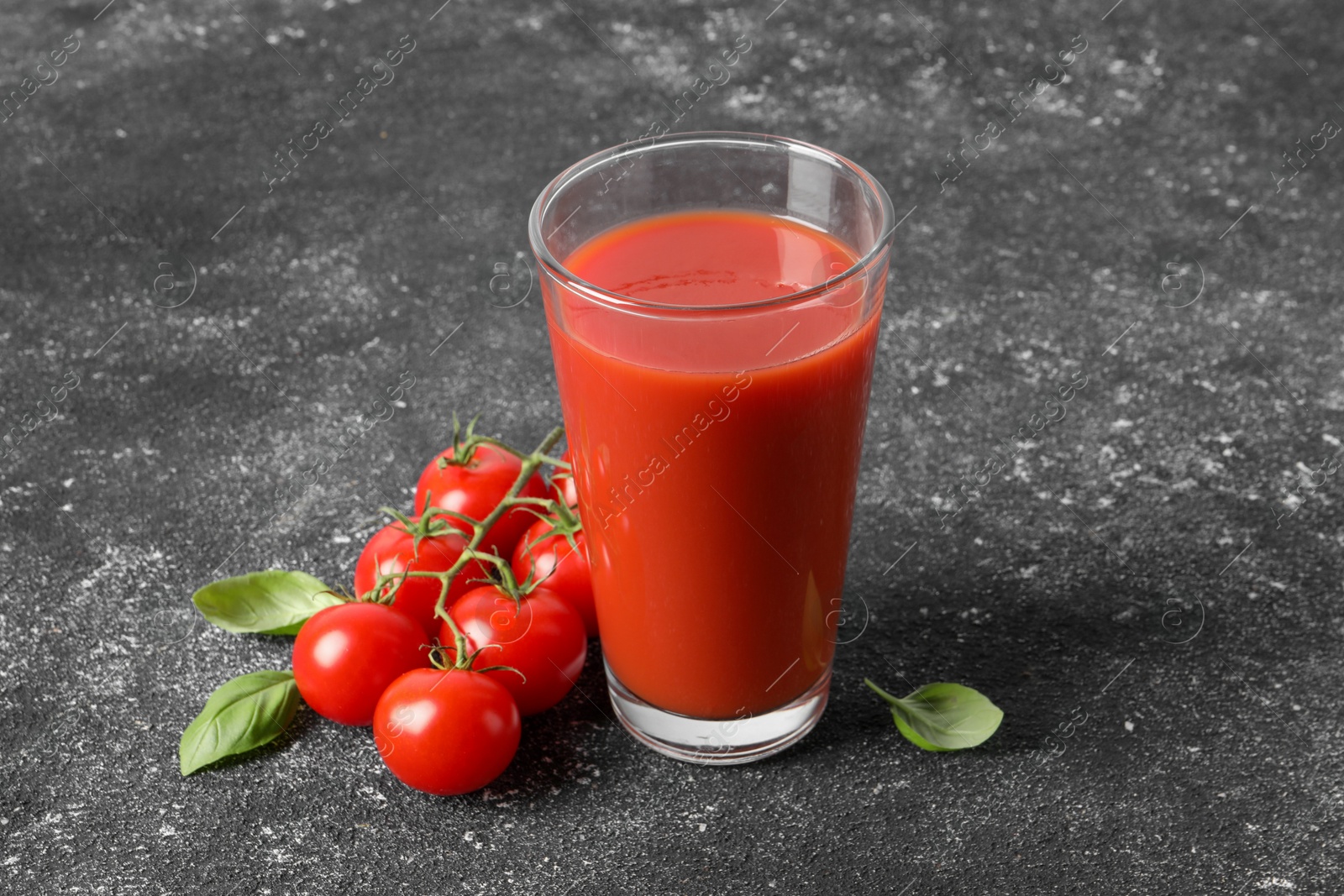 Photo of Tasty tomato juice in glass, basil and fresh vegetables on grey table