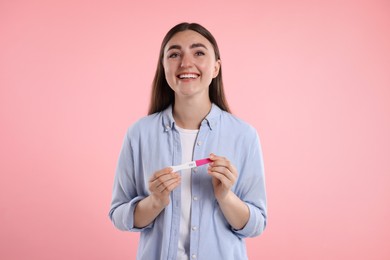Photo of Happy woman holding pregnancy test on pink background