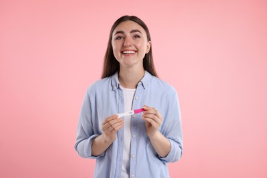 Happy woman holding pregnancy test on pink background