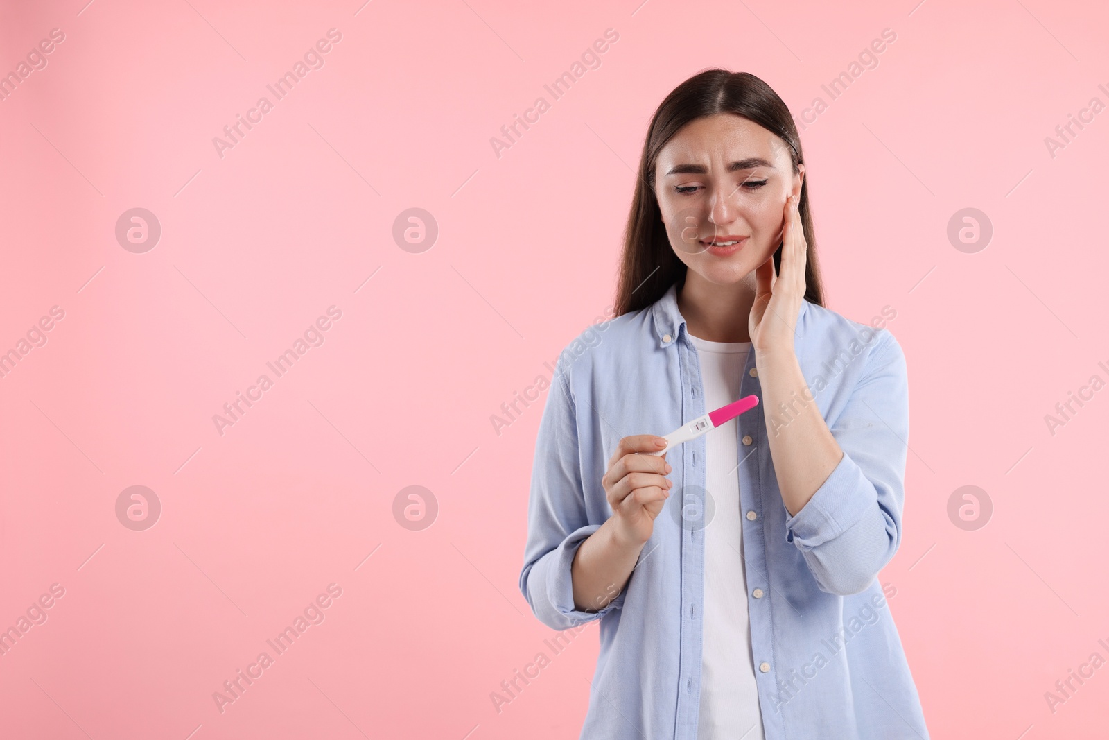 Photo of Sad woman holding pregnancy test on pink background, space for text