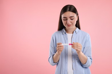 Photo of Sad woman holding pregnancy test on pink background, space for text