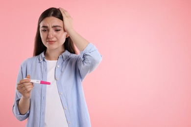 Photo of Sad woman holding pregnancy test on pink background, space for text