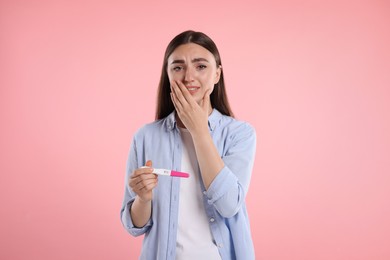 Sad woman holding pregnancy test on pink background