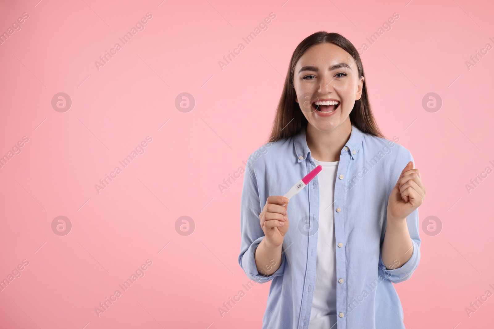 Photo of Happy woman holding pregnancy test on pink background, space for text