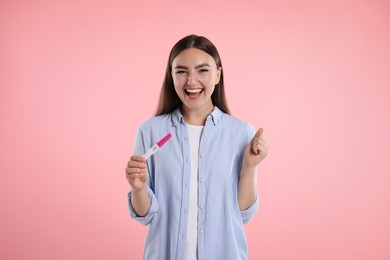 Happy woman holding pregnancy test on pink background