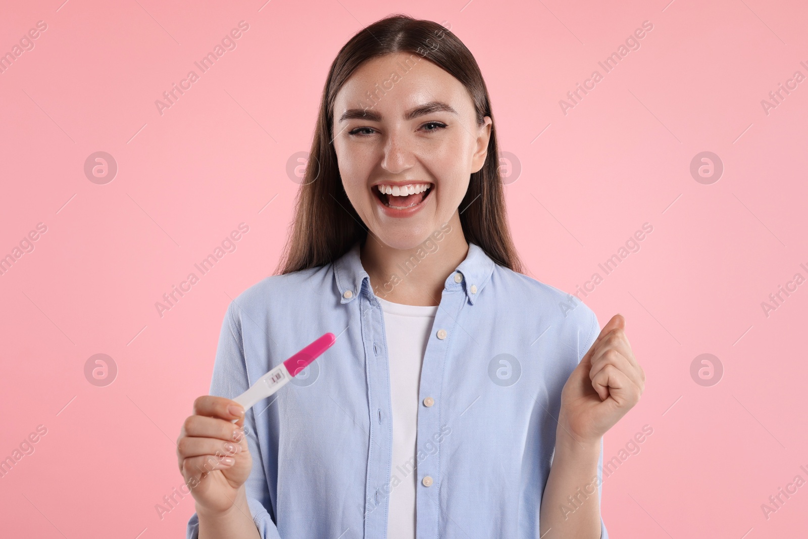 Photo of Happy woman holding pregnancy test on pink background