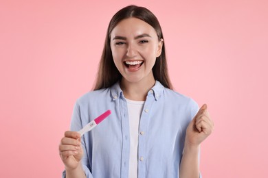 Photo of Happy woman holding pregnancy test on pink background