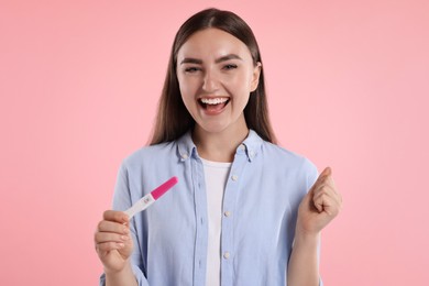 Happy woman holding pregnancy test on pink background