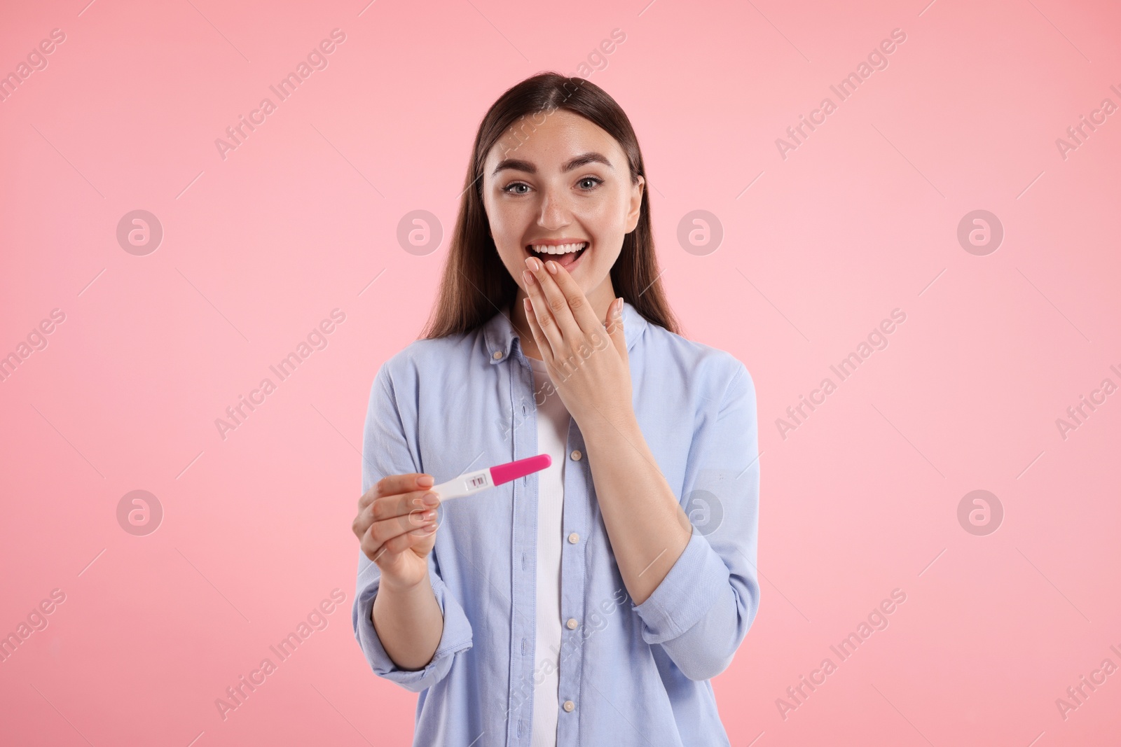 Photo of Happy woman holding pregnancy test on pink background