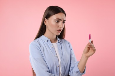 Confused woman holding pregnancy test on pink background