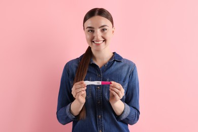 Photo of Happy woman holding pregnancy test on pink background