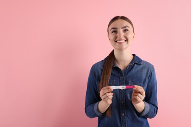 Happy woman holding pregnancy test on pink background, space for text