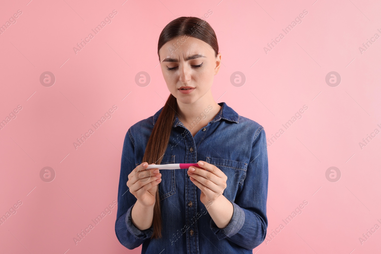 Photo of Confused woman holding pregnancy test on pink background