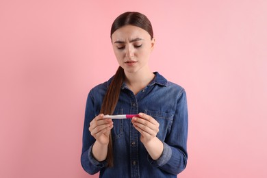 Confused woman holding pregnancy test on pink background