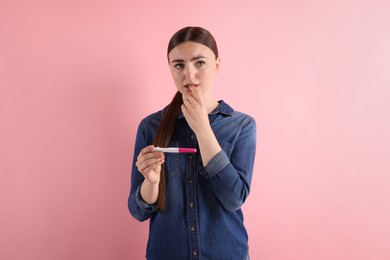 Confused woman holding pregnancy test on pink background