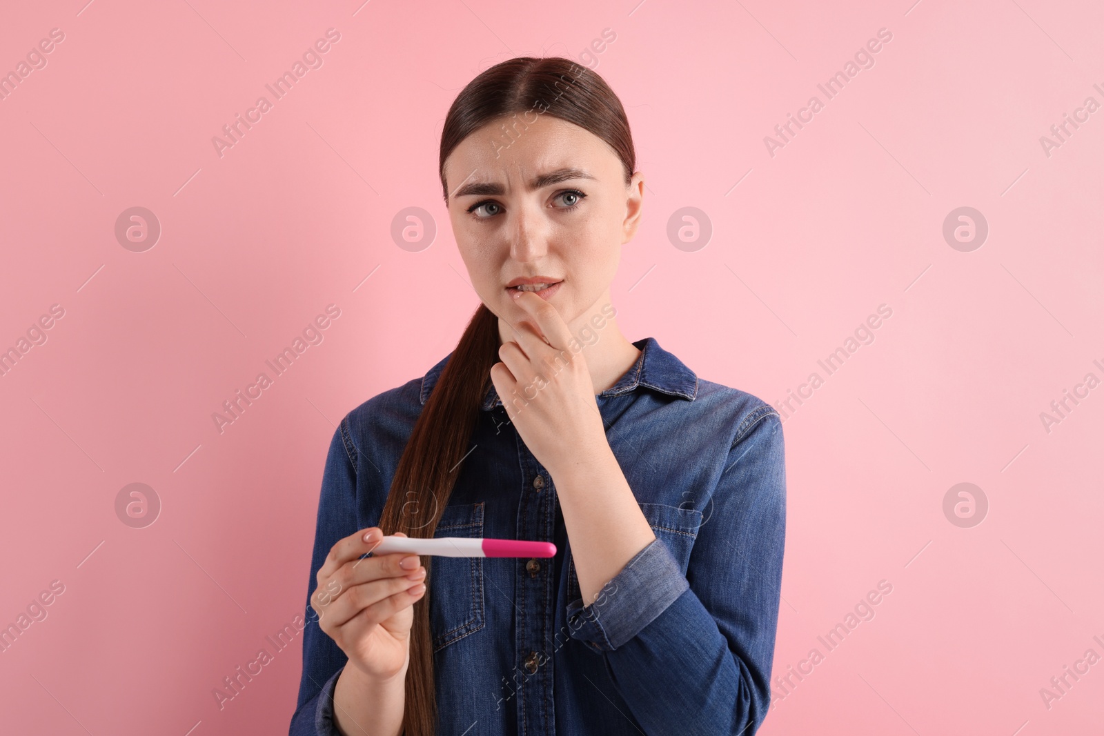 Photo of Confused woman holding pregnancy test on pink background