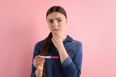 Confused woman holding pregnancy test on pink background