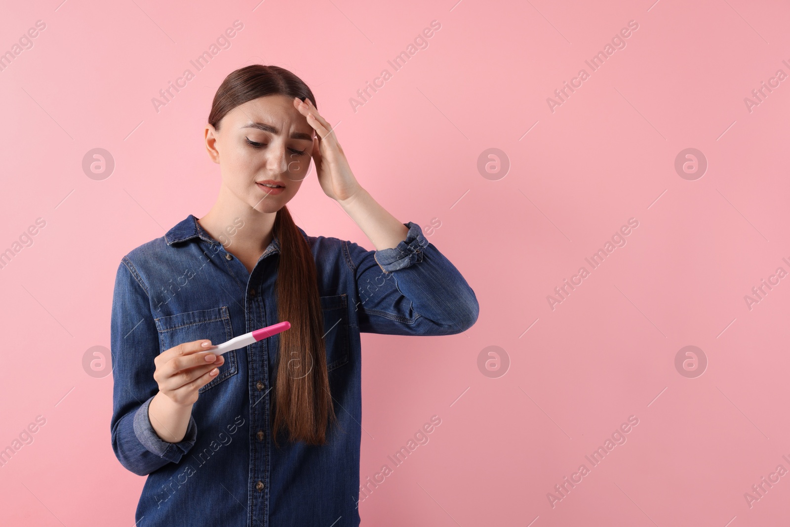 Photo of Confused woman holding pregnancy test on pink background, space for text