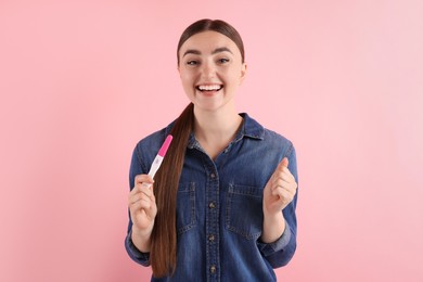 Happy woman holding pregnancy test on pink background