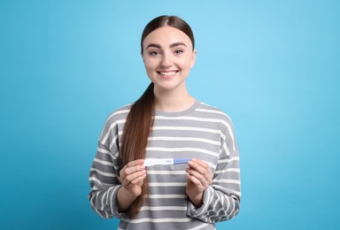 Happy woman holding pregnancy test on light blue background