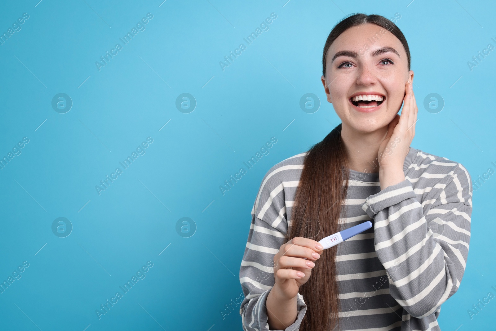 Photo of Happy woman holding pregnancy test on light blue background, space for text