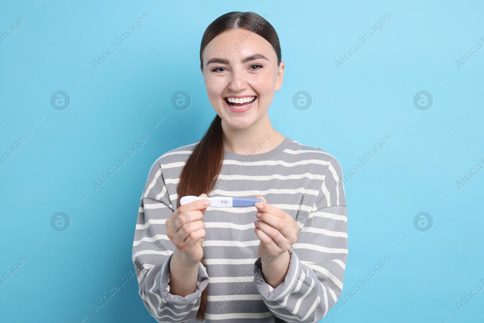 Photo of Happy woman holding pregnancy test on light blue background