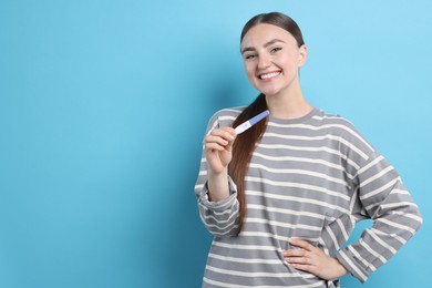 Happy woman holding pregnancy test on light blue background, space for text