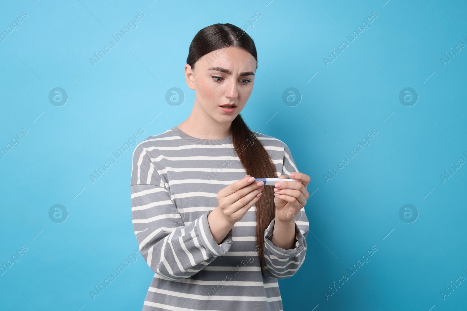 Photo of Shocked woman holding pregnancy test on light blue background