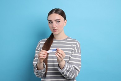 Photo of Shocked woman holding pregnancy test on light blue background