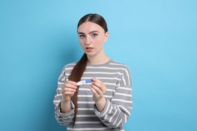 Shocked woman holding pregnancy test on light blue background