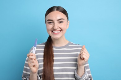 Happy woman holding pregnancy test on light blue background