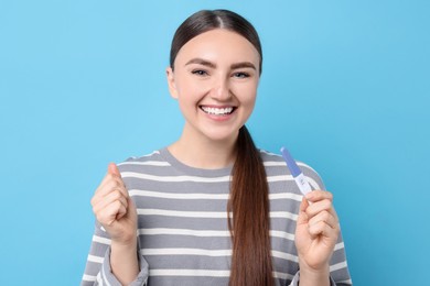 Photo of Happy woman holding pregnancy test on light blue background