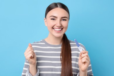 Happy woman holding pregnancy test on light blue background