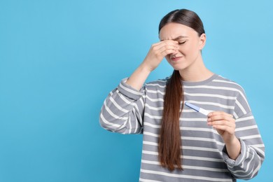 Sad woman holding pregnancy test on light blue background, space for text