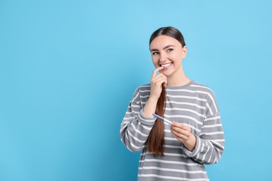 Photo of Happy woman holding pregnancy test on light blue background, space for text