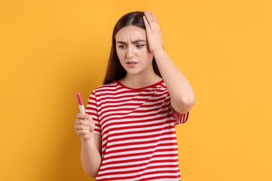 Photo of Confused woman holding pregnancy test on orange background