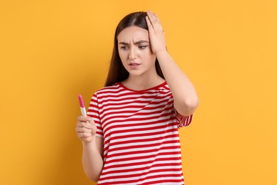 Confused woman holding pregnancy test on orange background