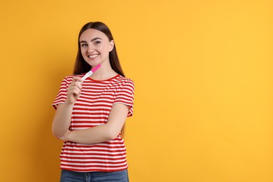 Photo of Happy woman holding pregnancy test on orange background, space for text