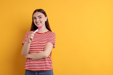 Happy woman holding pregnancy test on orange background, space for text