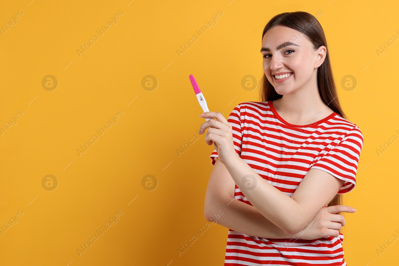 Photo of Happy woman holding pregnancy test on orange background, space for text