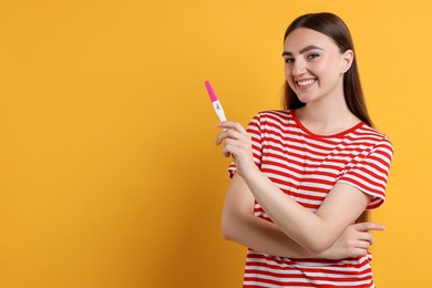 Happy woman holding pregnancy test on orange background, space for text