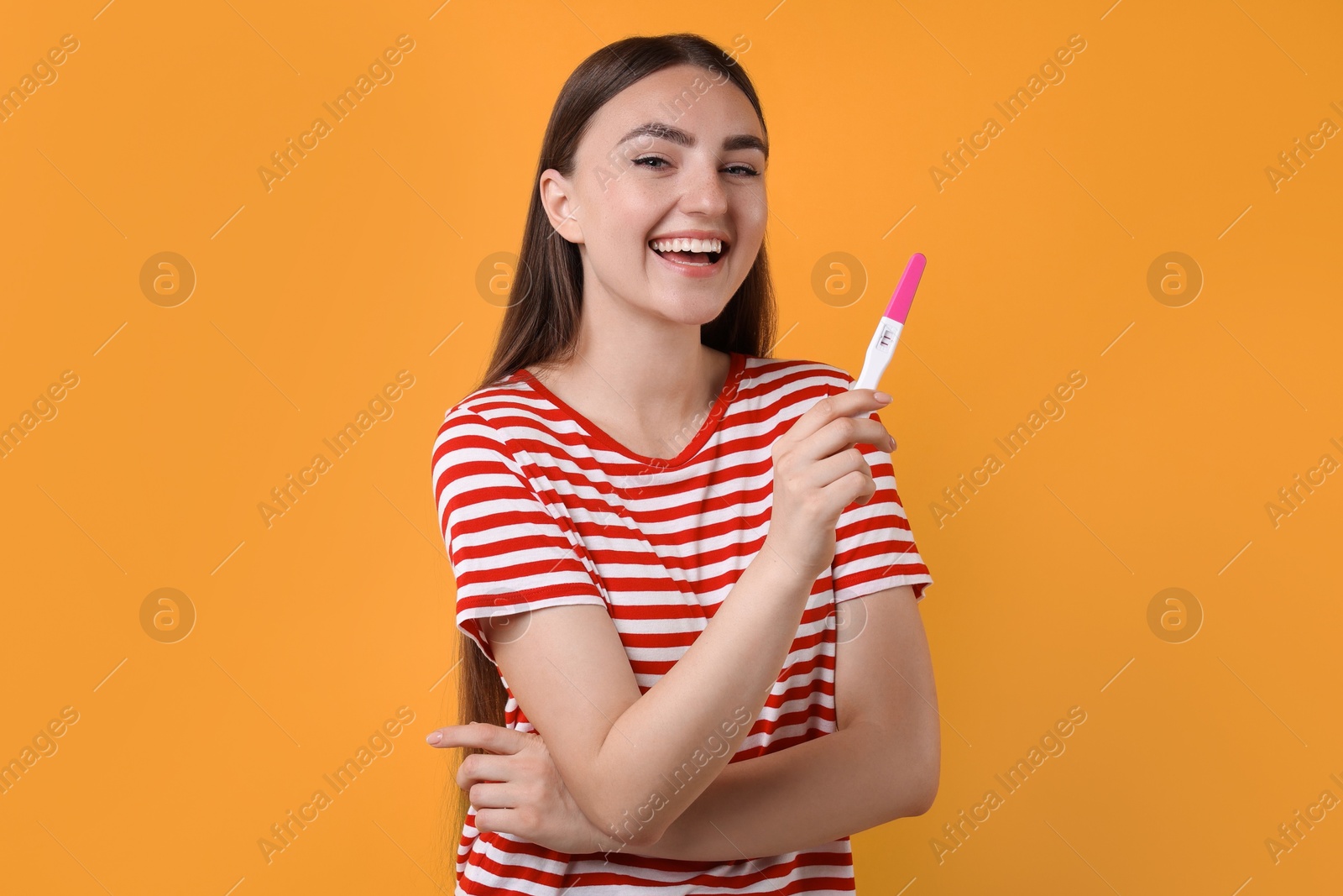 Photo of Happy woman holding pregnancy test on orange background