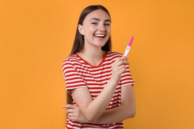 Happy woman holding pregnancy test on orange background